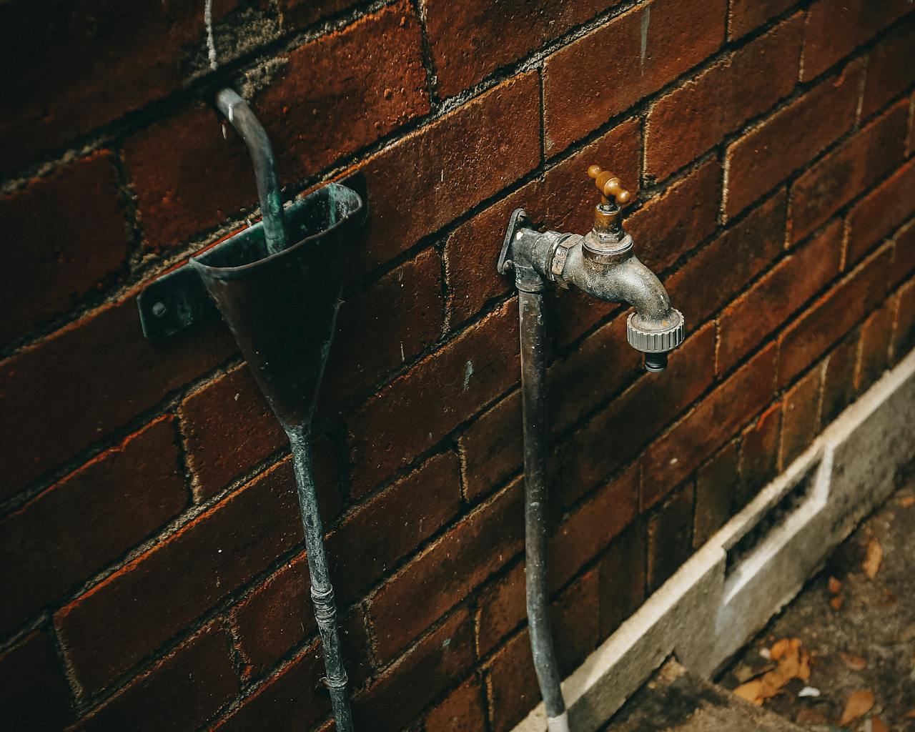 services-05 Close-up of a rusty outdoor faucet attached to a weathered brick wall.
