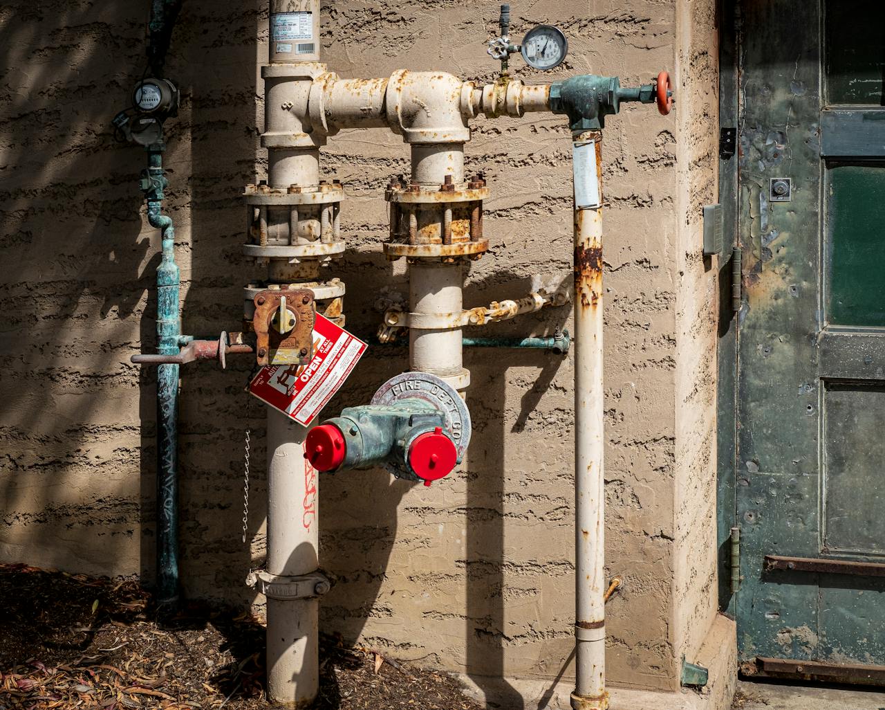 story-02 Rusty outdoor plumbing pipes with pressure gauges and warning signs on a wall.